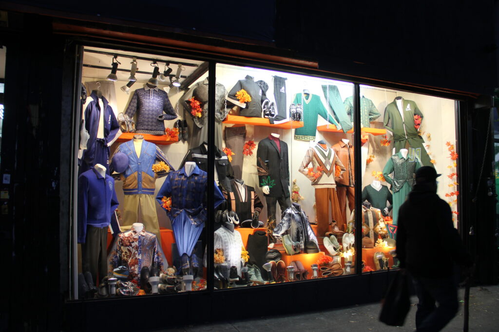 A silhouetted person walks past an illuminated store window displaying clothing for sale.
